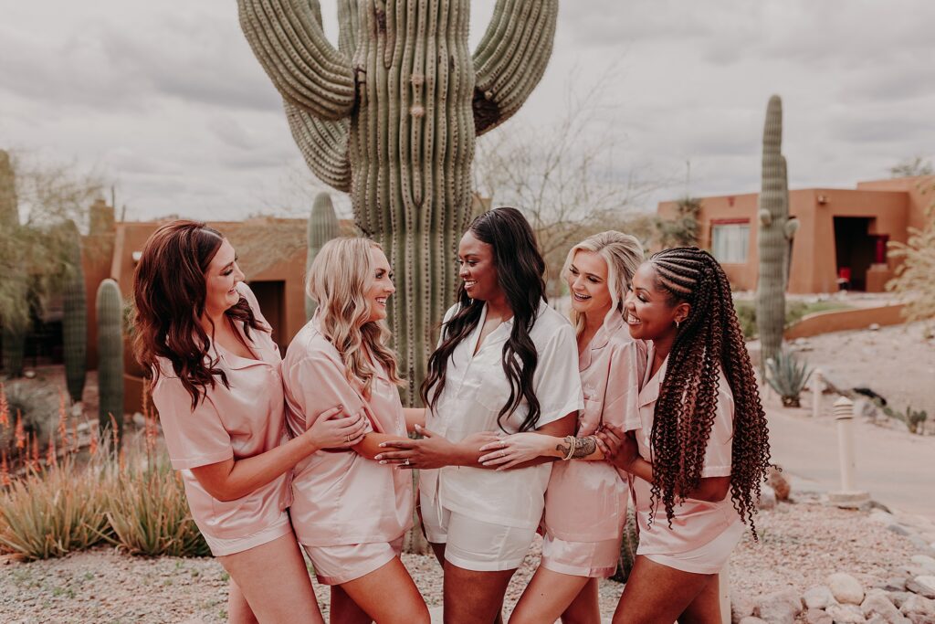 bride and bridesmaids wear matching pjs and stand in front of a saguaro 
