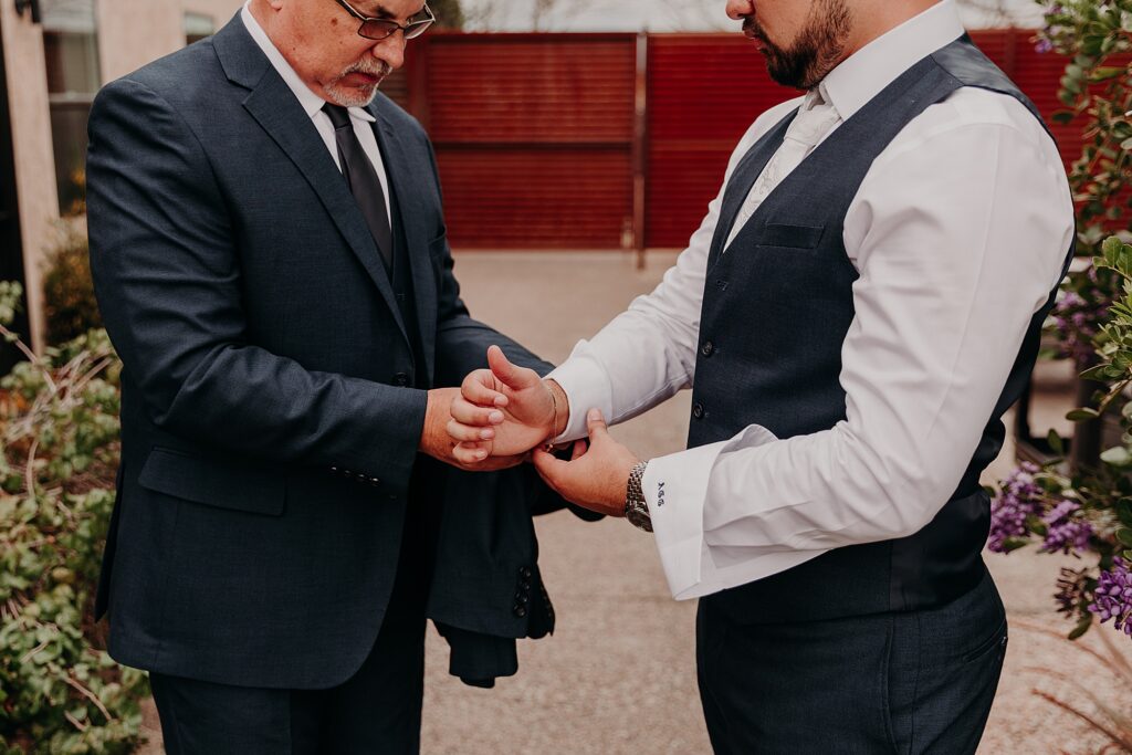 father helps groom put on suit and jacket on wedding day