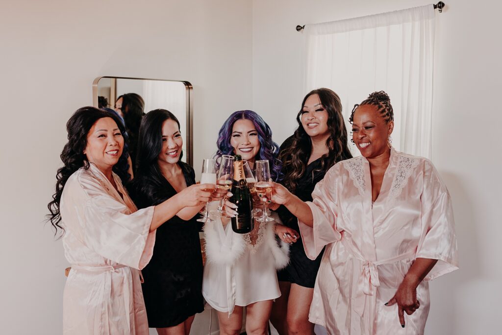bride and her bridesmaids pour champagne and cheers their glasses