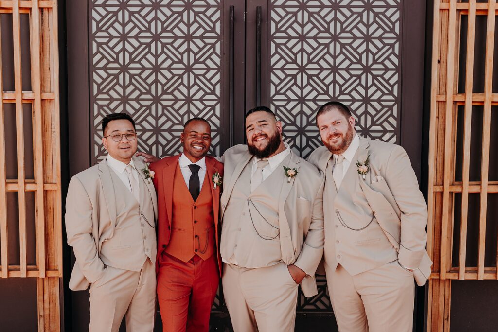 groomsmen pose in terracotta and tan suits again mosaic doors
