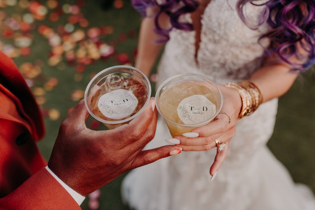 bride and groom hold signature cocktails and cheers their drinks