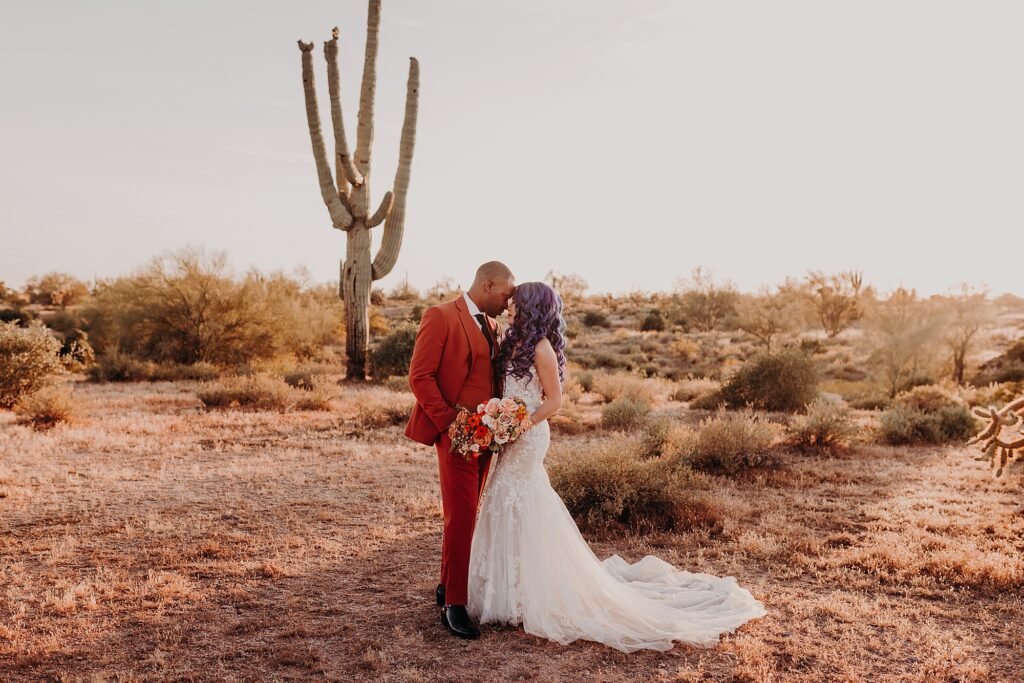 bride and groom cuddle and nuzzle noses in the desert