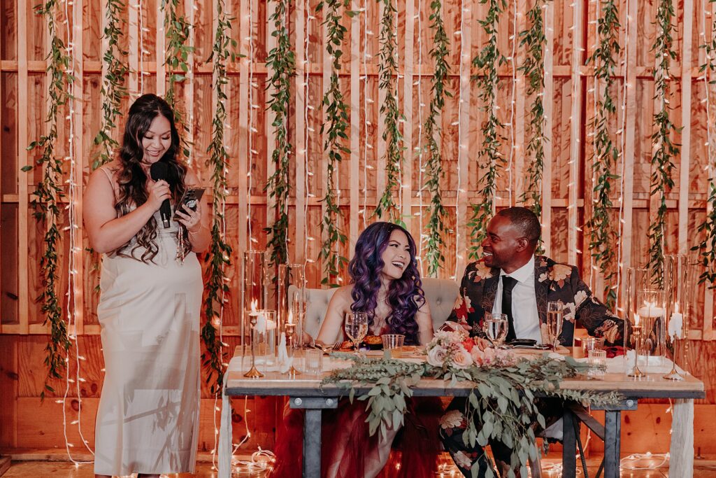 bride and groom laugh and listen as maid of honor shares wedding toast