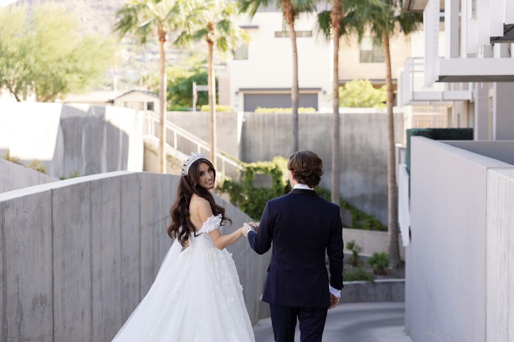 bride and groom walk hand in hand away from the camera and brides looks over her shoulder