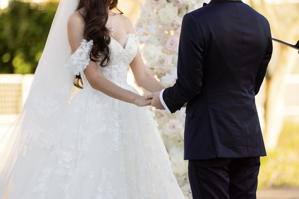 groom and bride hold hands during wedding ceremony