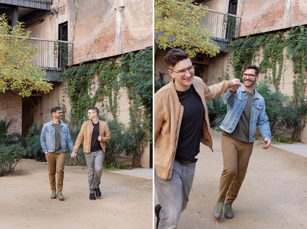 Couple skips hand in hand towards the camera smiling in ivy covered historic courtyard.