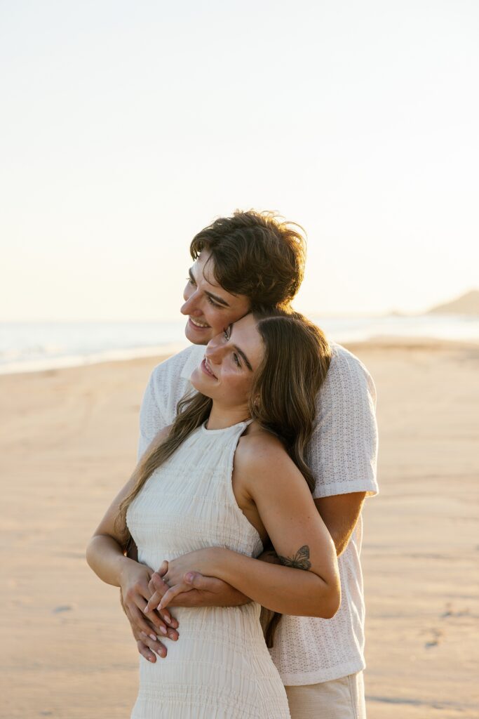 couple romantically cuddle and watch the sunset on a beach in rocky point