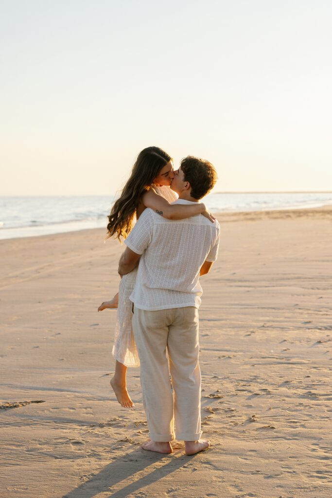man lifts and spins his fiance on the beach after proposing