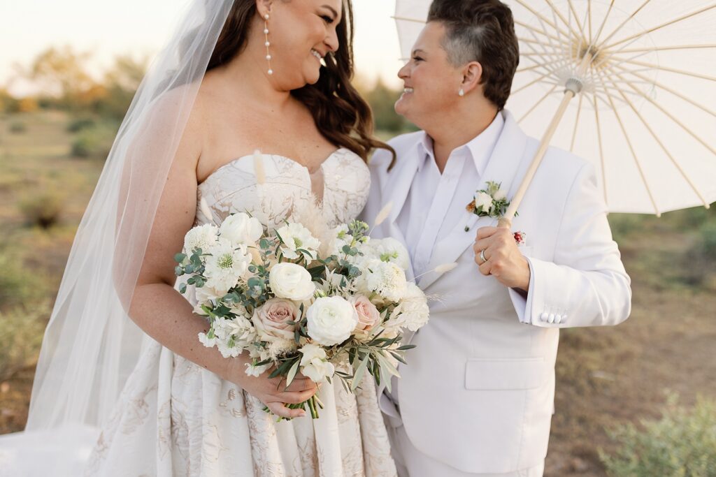 Two brides at sunset holding flowers in the Apache Junction desert at the Paseo wedding venue.