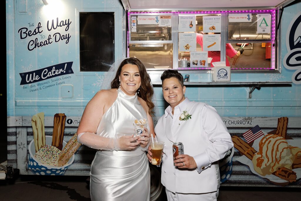 Two brides share ice cream floats from food truck at wedding.