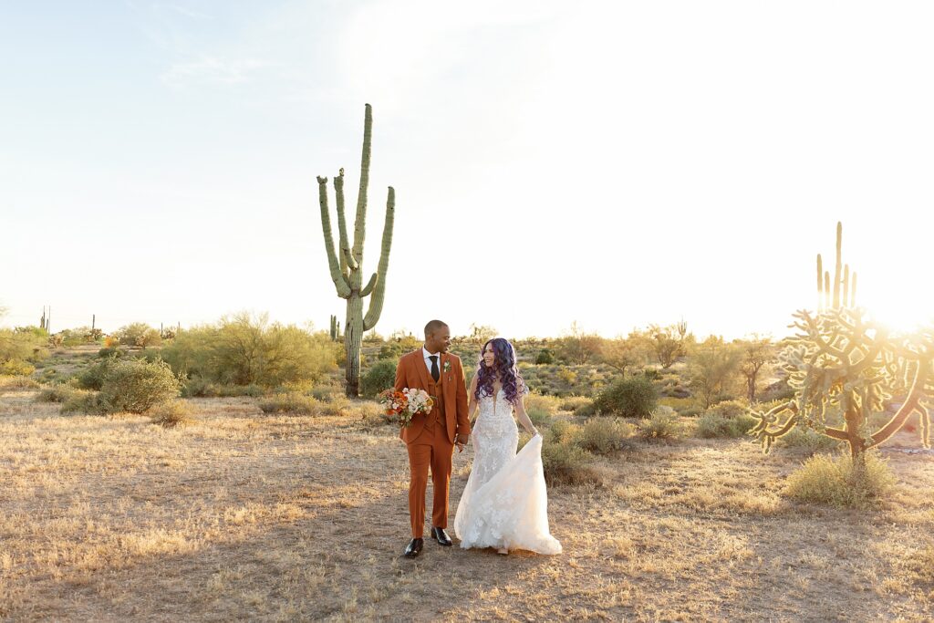Bride and groom walk hand in hand through the desert at sunset at the Paseo Wedding Venue.