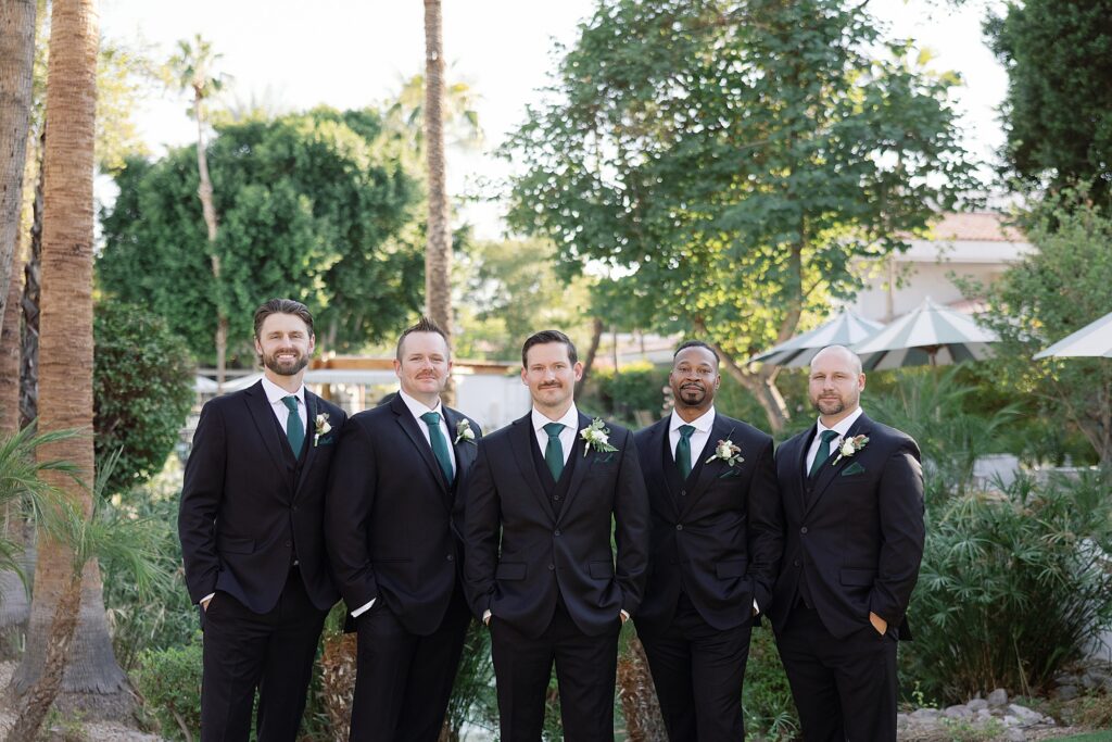 Groom and groomsmen smile in front of palm trees at the Scott Resort and Spa.
