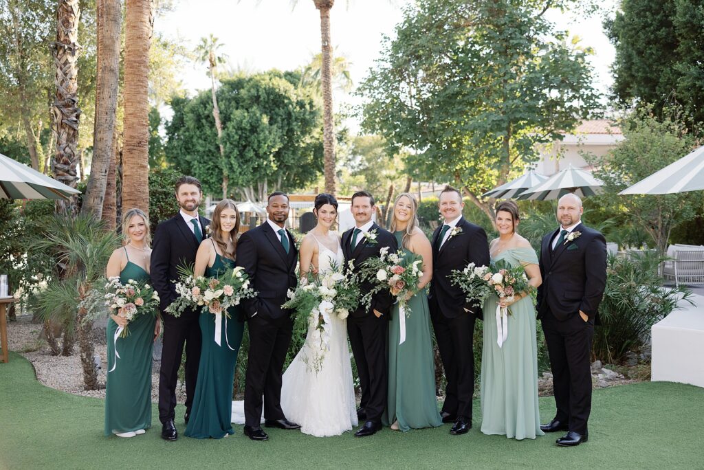 Wedding party smiles in green attire in front of palm trees at the Scott Resort and Spa.