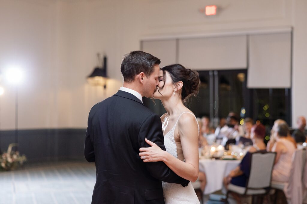 Bride and groom share kiss during first dance at wedding reception.