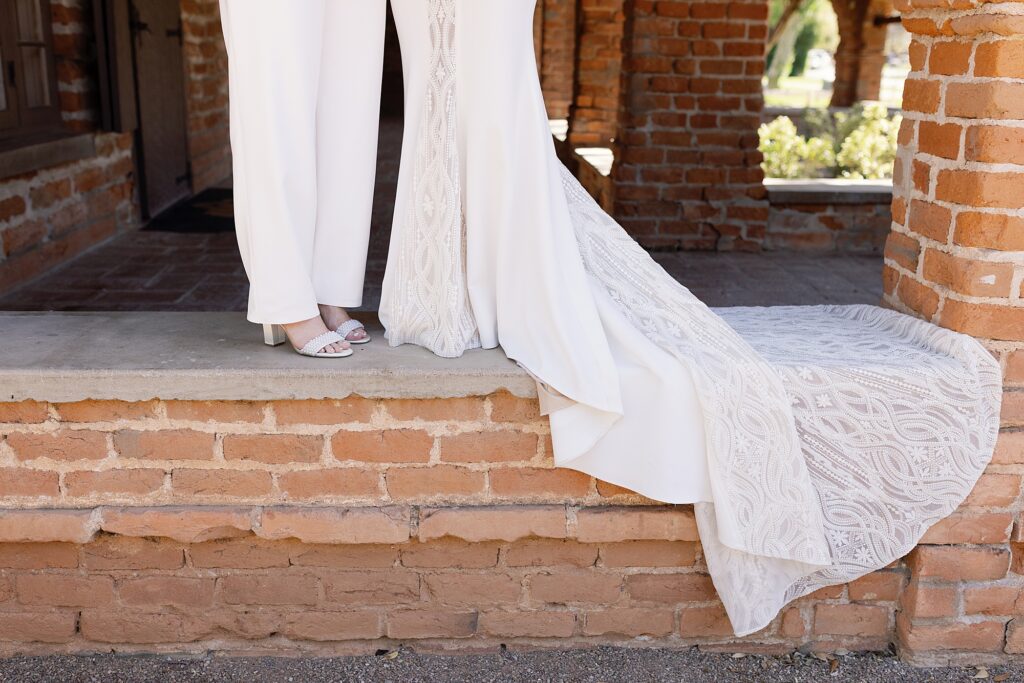 Two brides stand together under red brick archway on wedding day at the Tubac Resort and Spa.