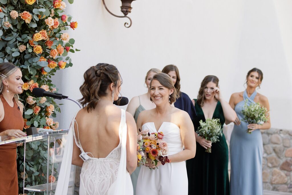 Two brides smile at each other during wedding ceremony in Tubac. 