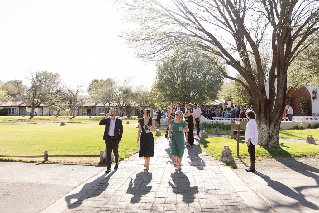 Wedding guests walk across sunny lawn after ceremony.