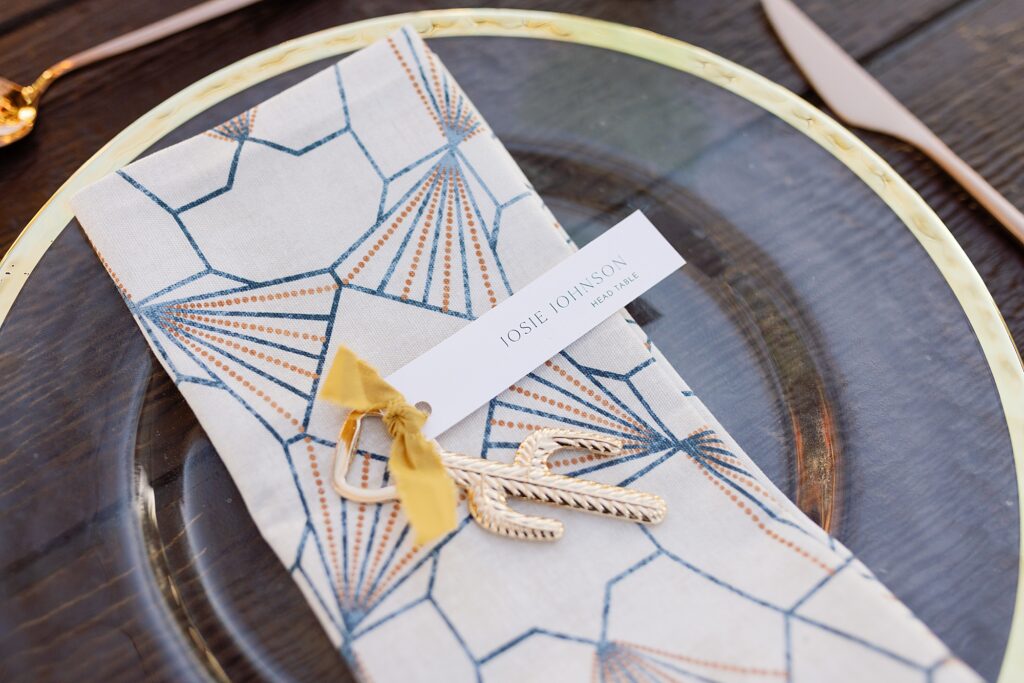 Wedding dinner place setting with gold cactus bottle opener on geometric napkin.