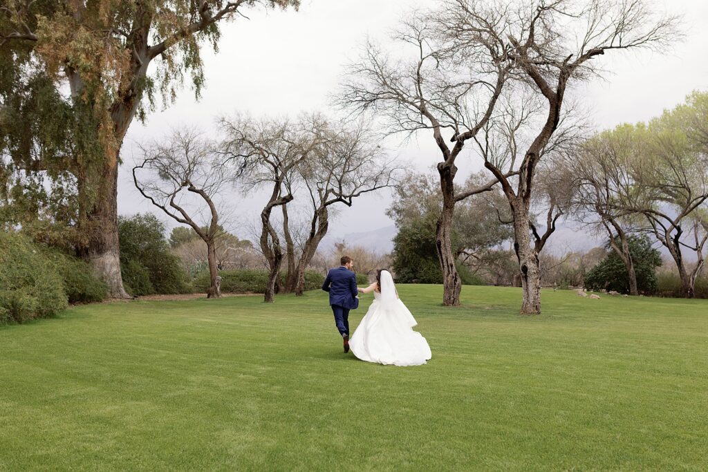 bride and groom run away from the camera through a field of grass and trees