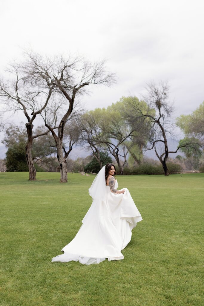 bride holds up wedding gown while running away in a field of grass