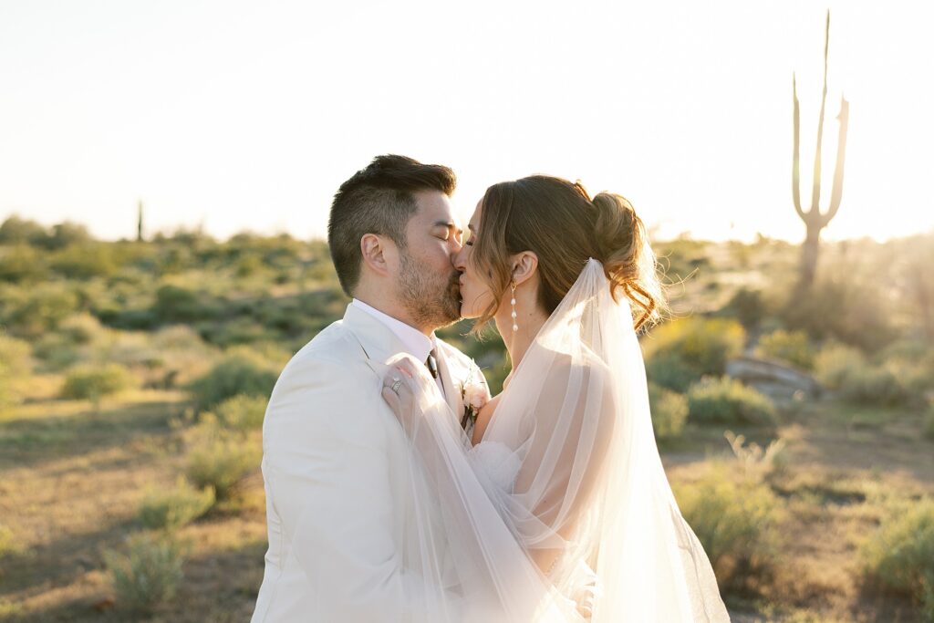 bride and groom kiss in the desert at sunset