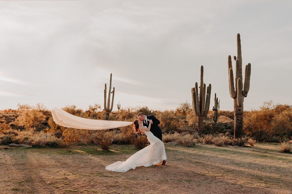 groom dips bride in the desert at sunset