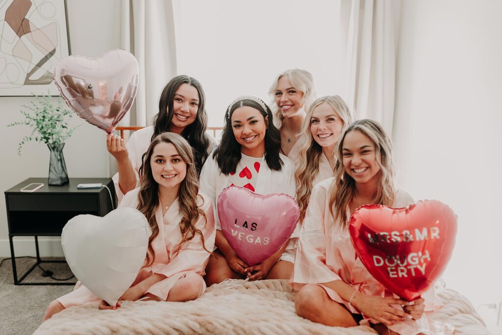 Bride and bridesmaids sitting on bed holding balloons