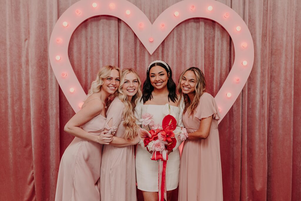 bride and bridesmaids stand in front of pink backdrop at sure thing chapel