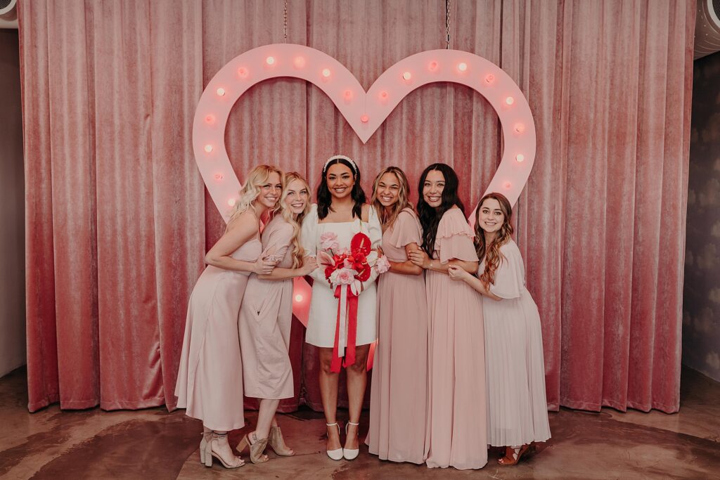 bride and bridesmaids stand in front of pink backdrop at sure thing chapel